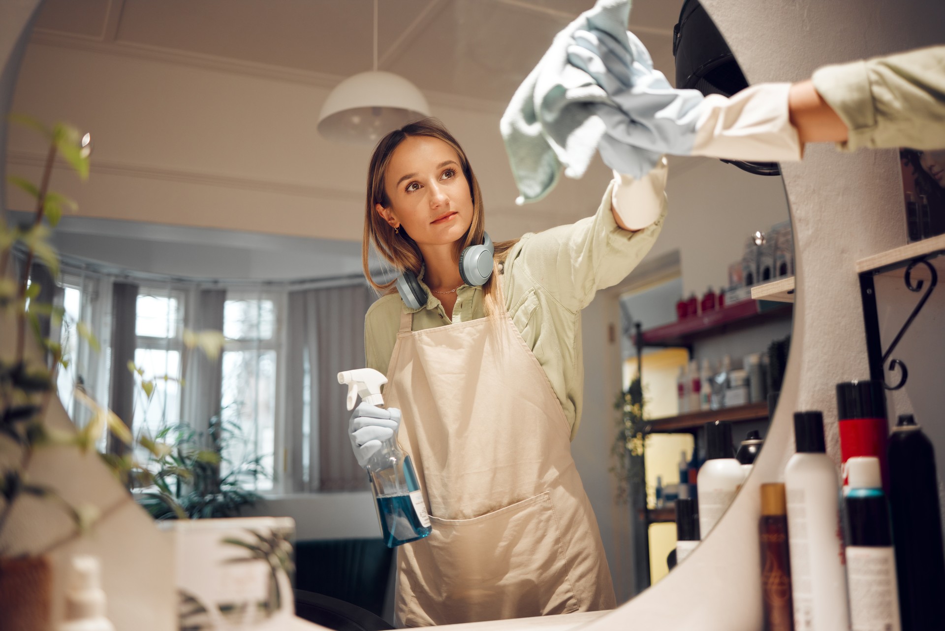 Cleaning, bathroom and mirror with a woman washing glass in a house for hygiene with disinfectant or polish. Cloth, housework and gloves with a female cleaner doing housekeeping in a domestic home